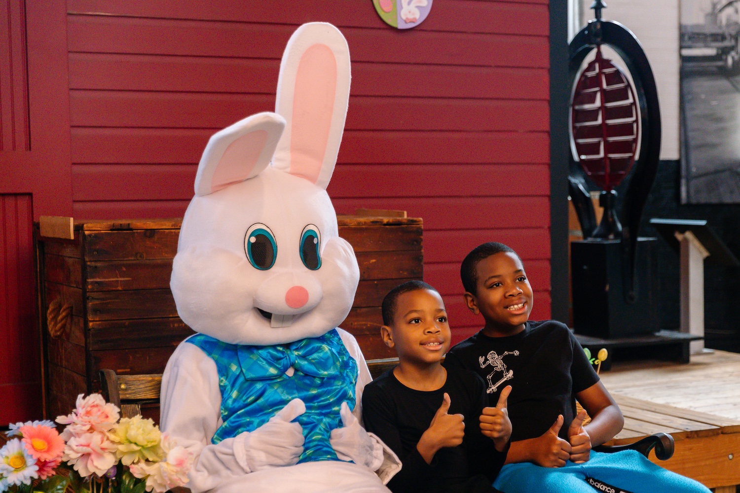 Two children giving a thumbs up sit next to the Easter Bunny